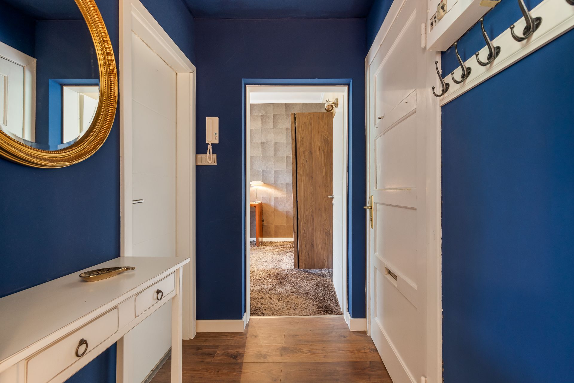 Flur mit blauen Wänden, weißer Kommode, Spiegel und Garderobe, Türen zu anderen Räumen.