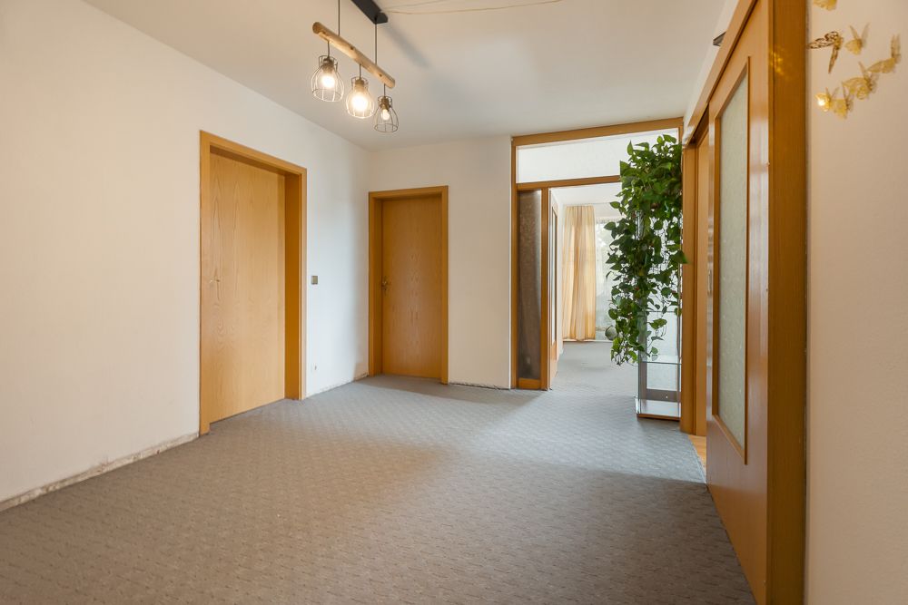 Heller Flur mit Teppichboden, Holztüren und einer großen Zimmerpflanze im Hintergrund.