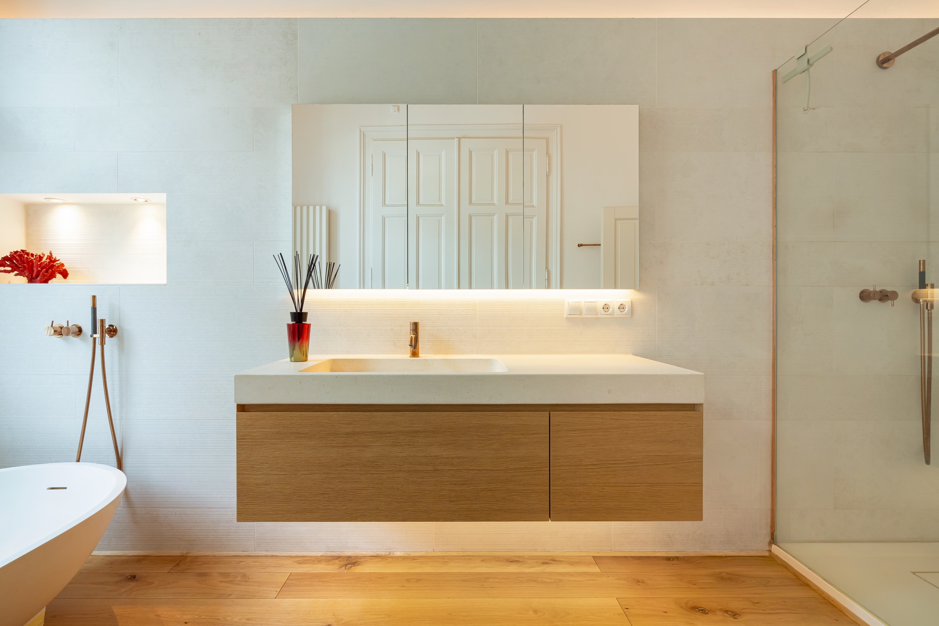 Modernes Bad mit Spiegel, Holzwaschtisch, Glasdusche und Badewanne auf Holzboden.