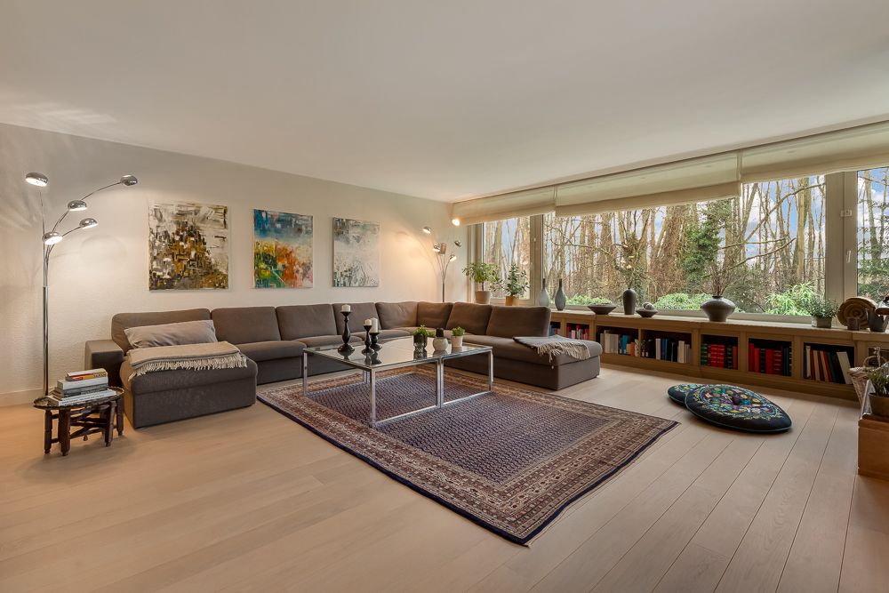 Helles Wohnzimmer mit großer Eckcouch, Teppich, großen Fenstern und Regalen mit Büchern.