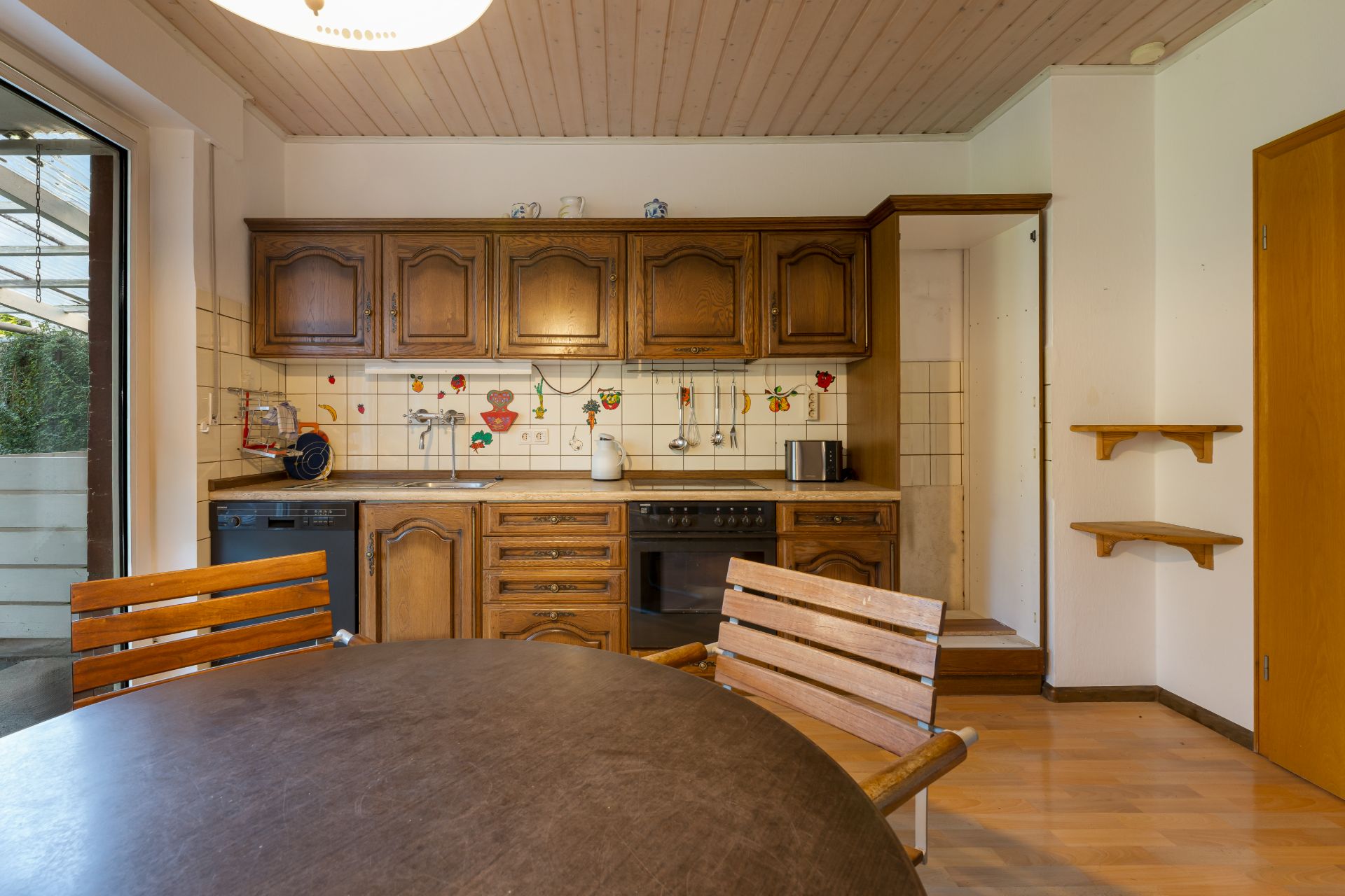 Küche mit Holzmöbeln, rundem Tisch und Wandfliesen mit Blumenmotiven.