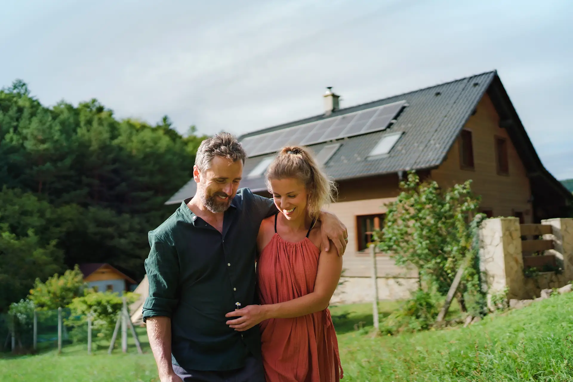Ein Paar geht lachend im Garten vor einem Haus mit Solarpanels auf dem Dach.