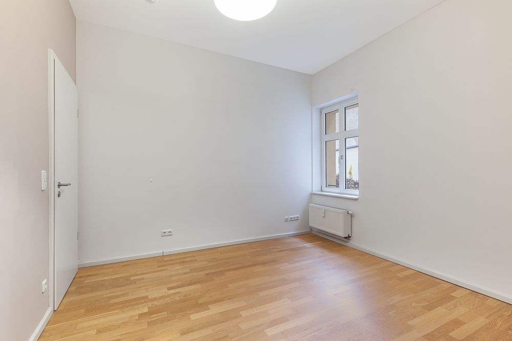 Leerer Raum mit Holzfußboden, weißer Wand, Tür und Fenster mit Heizung darunter.