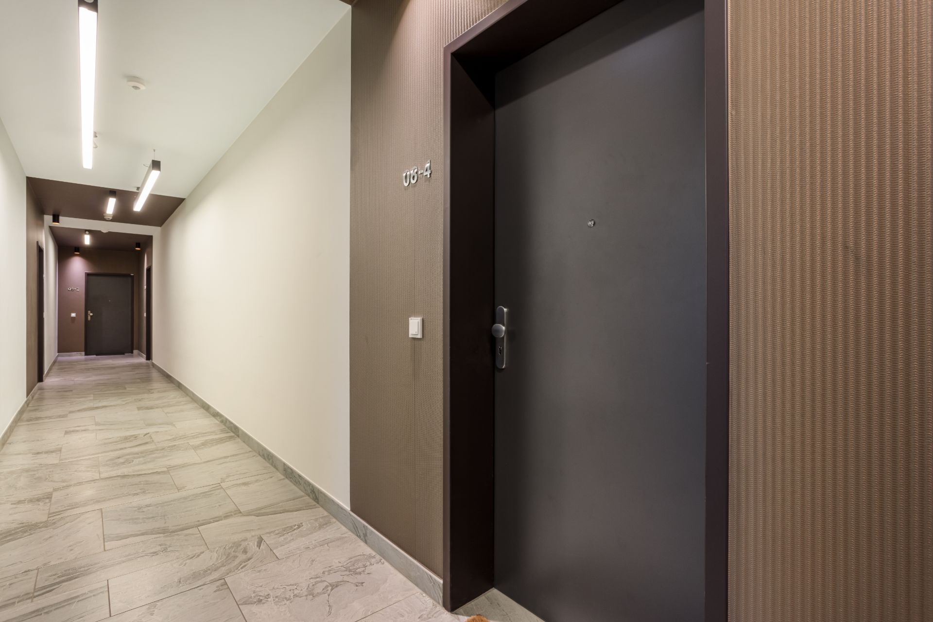 Moderner Wohnungsflur mit hellen Wänden, Fliesenboden und mehreren dunklen Wohnungstüren.