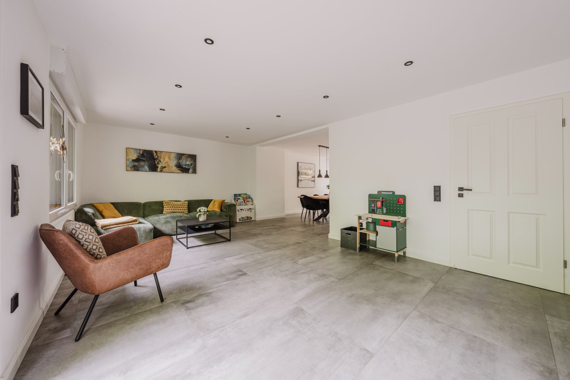 Helles Wohnzimmer mit Sofa, Sessel, Spielküche und Blick in ein Esszimmer.