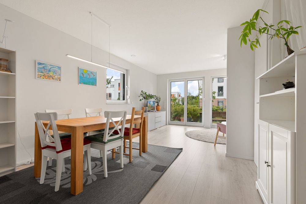 Helles Wohnzimmer mit Esstisch, weißen Stühlen und großen Fenstern zum Garten.