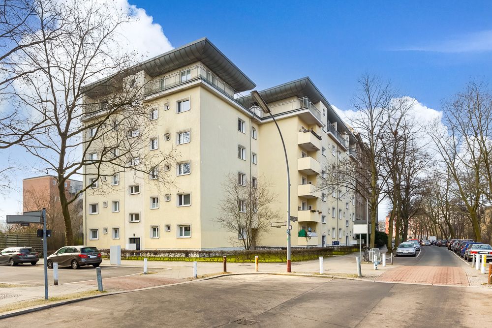 Mehrstöckiges Wohngebäude an einer Straßenecke mit Balkonen und geparkten Autos.
