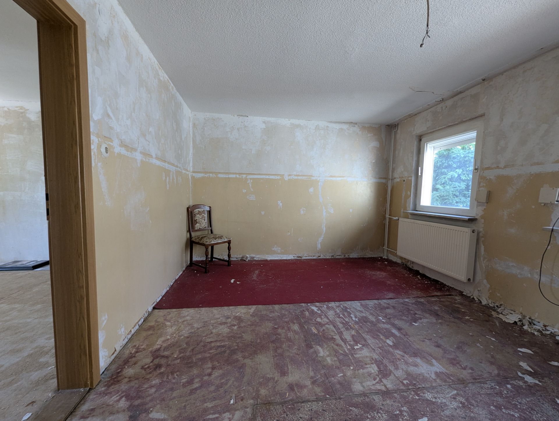 Leerer, renovierungsbedürftiger Raum mit einem Stuhl, Fenster und sichtbaren Wandspuren.