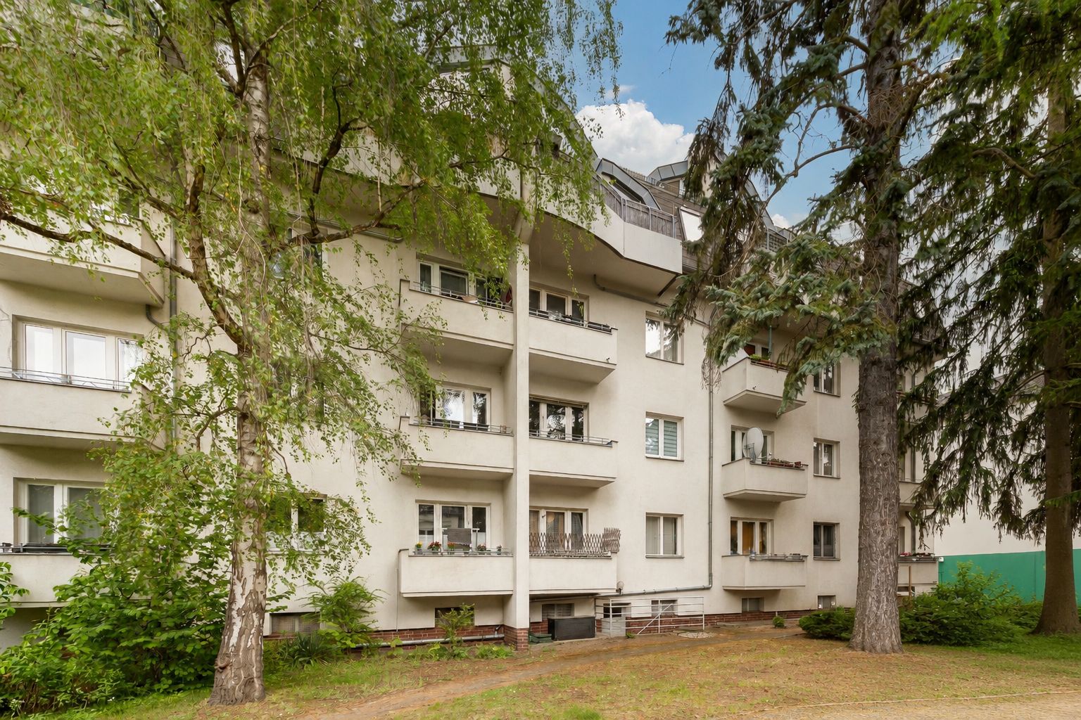 Mehrfamilienhaus mit Balkonen und Bäumen im Vorgarten.