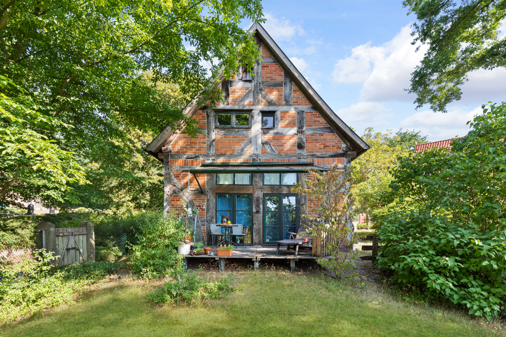 Fachwerkhaus mit Terrasse, Pflanzen und Garten im Vordergrund.
