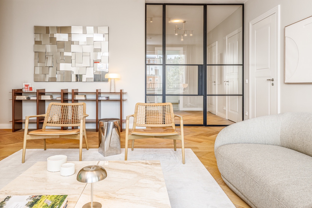 Modernes Wohnzimmer mit zwei Stühlen, Sofa, Couchtisch, Wandspiegel und Glastrennwand.