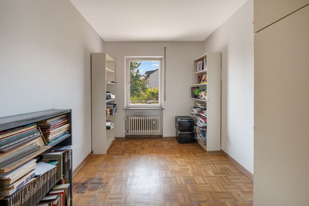Helles Zimmer mit Parkettboden, Bücherregalen und einem Fenster mit Blick nach draußen.