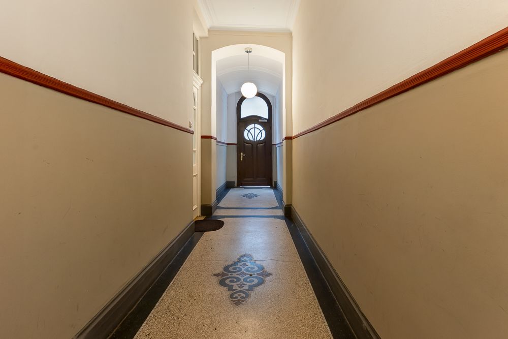 Langer Flur mit verziertem Boden und brauner Holztür am Ende.