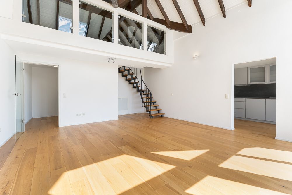 Helles Wohnzimmer mit Holzfußboden, offener Küche, Treppe zur Galerie und sichtbaren Holzbalken.
