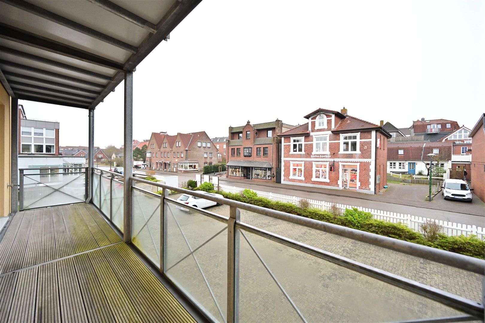 Balkon mit Holzboden und Metallgeländer, Blick auf eine ruhige Wohnstraße mit Häusern.