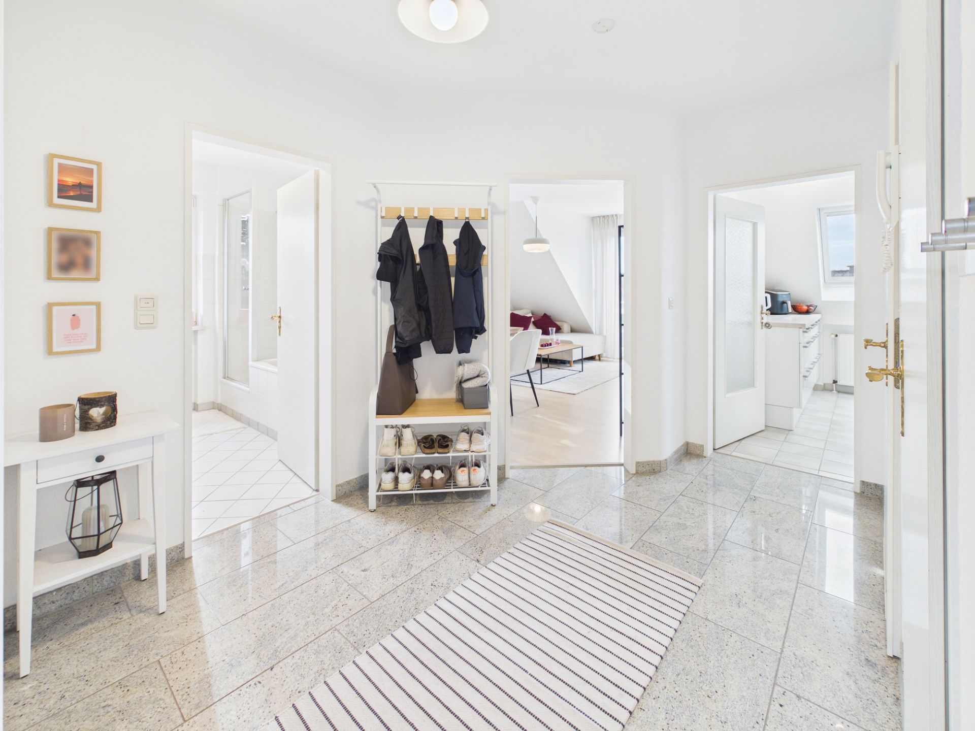 Heller Flur mit Garderobe, Schuhregal, Teppich und Blick in Wohn- und Küchenbereich.