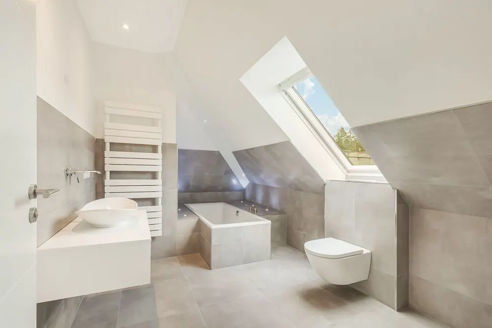 Modernes Badezimmer mit Badewanne, Waschbecken, Wandtoilette und großem Dachfenster.