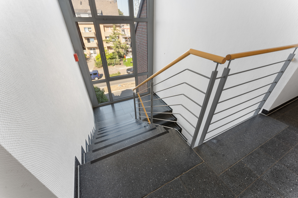 Treppenhaus mit Geländer und großem Fenster, Blick nach draußen auf eine Straße.
