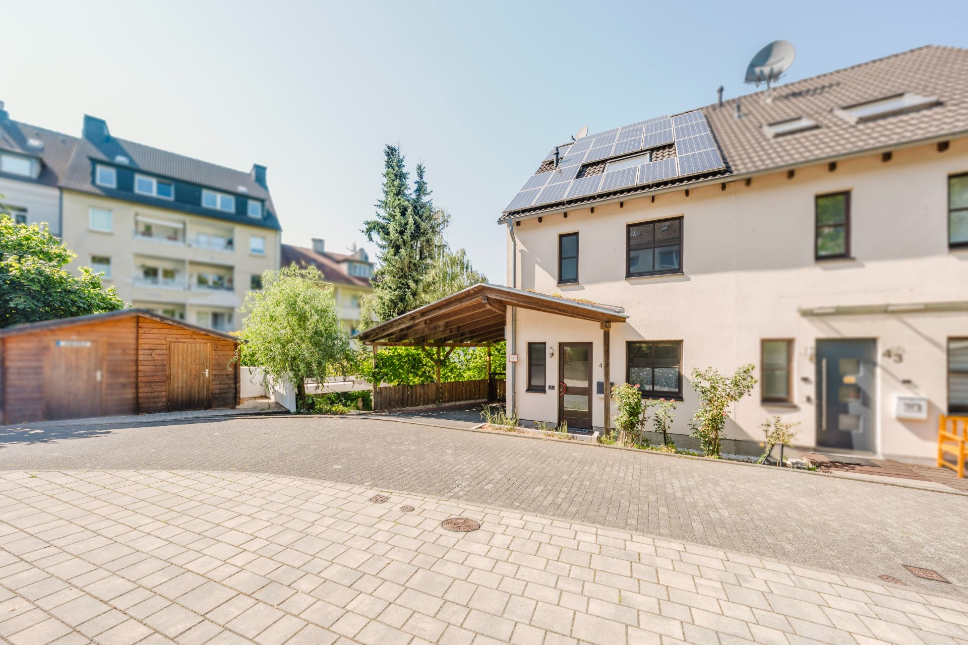 Modernes Wohnhaus mit Solarpanels, Carport und gepflasterter Einfahrt.