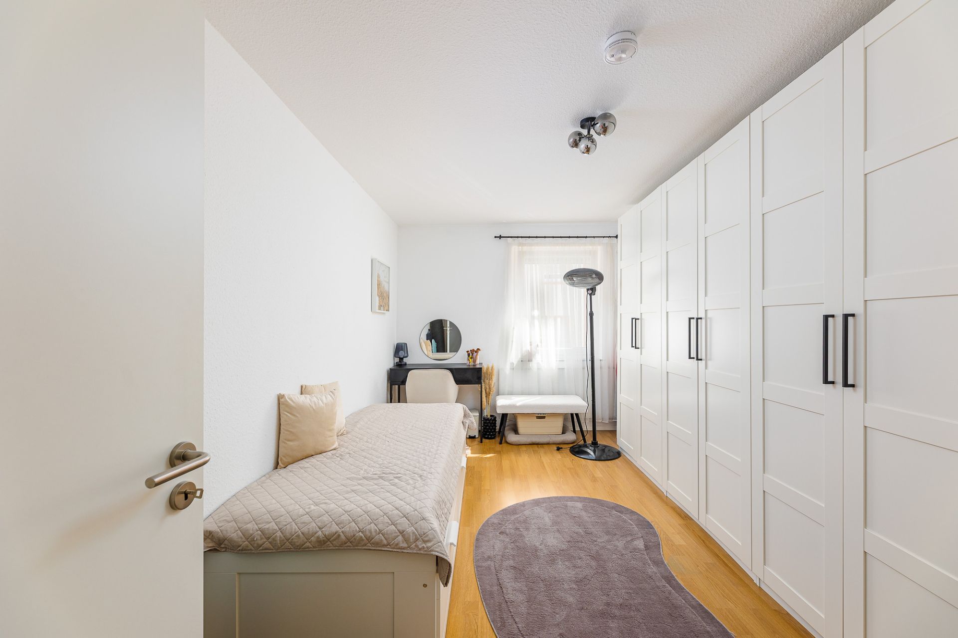 Helles Schlafzimmer mit Einzelbett, großem Kleiderschrank und Schreibtisch am Fenster.