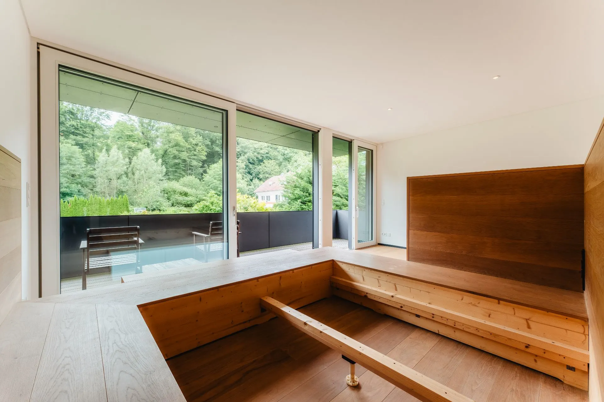 Modernes Wohnzimmer mit Holzsitzbank und großen Fenstern zur Terrasse mit Blick ins Grüne.