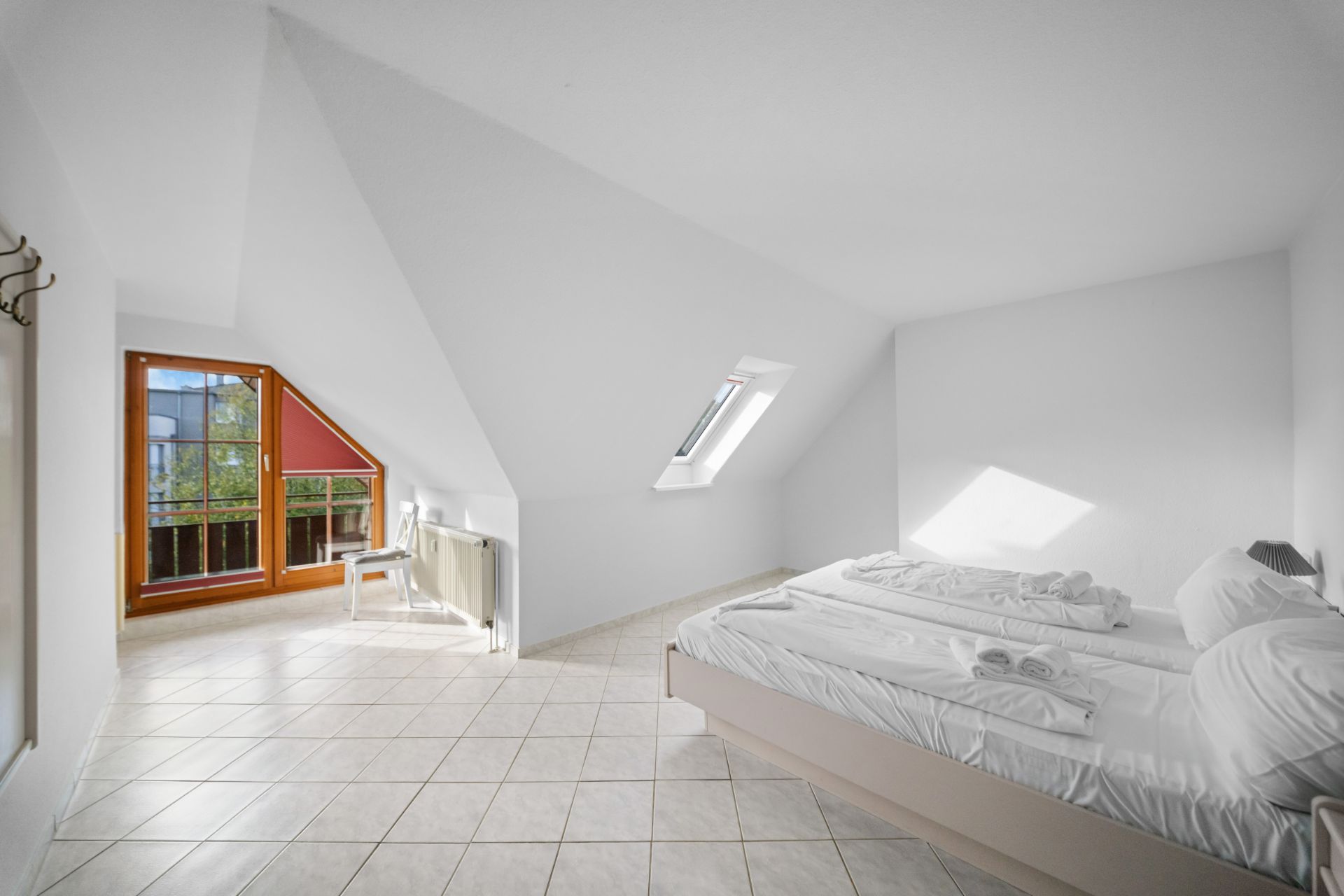 Helles Schlafzimmer mit Doppelbett, Fenster im Dach und Zugang zu einem Balkon.
