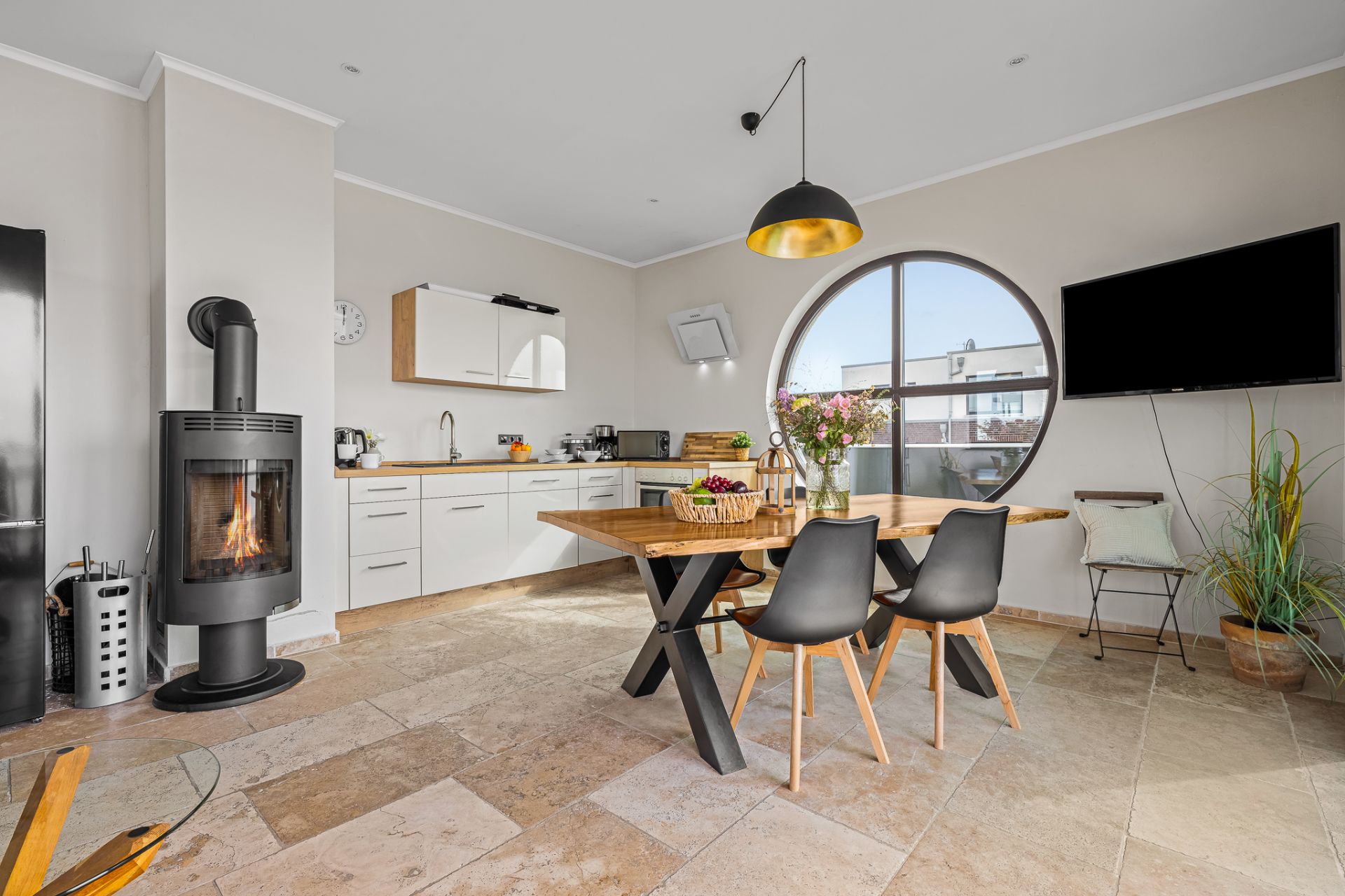 Moderne Küche mit Esstisch, Kaminofen, rundem Fenster und Wandfernseher.
