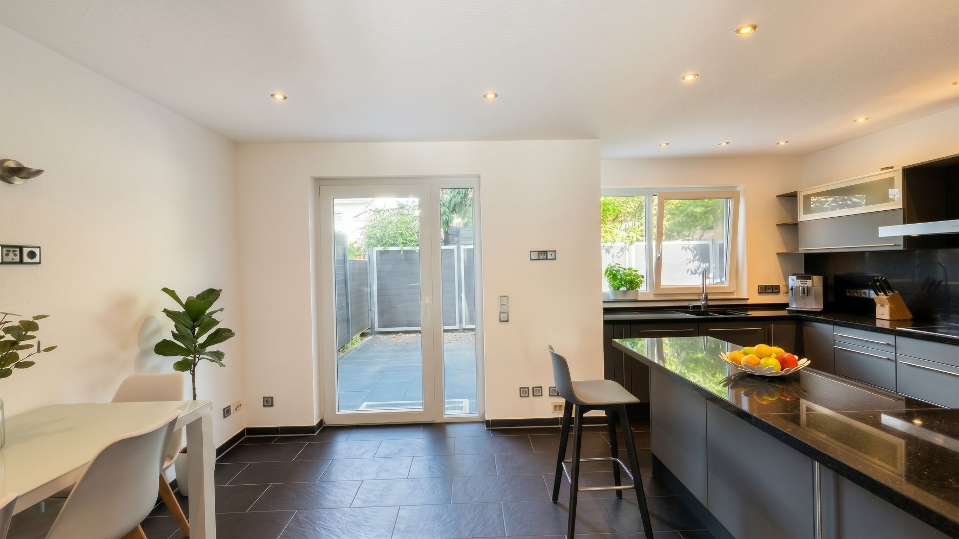 Moderne Küche mit Inseltresen, Essbereich, großen Fenstern und Glas­tür zum Garten.