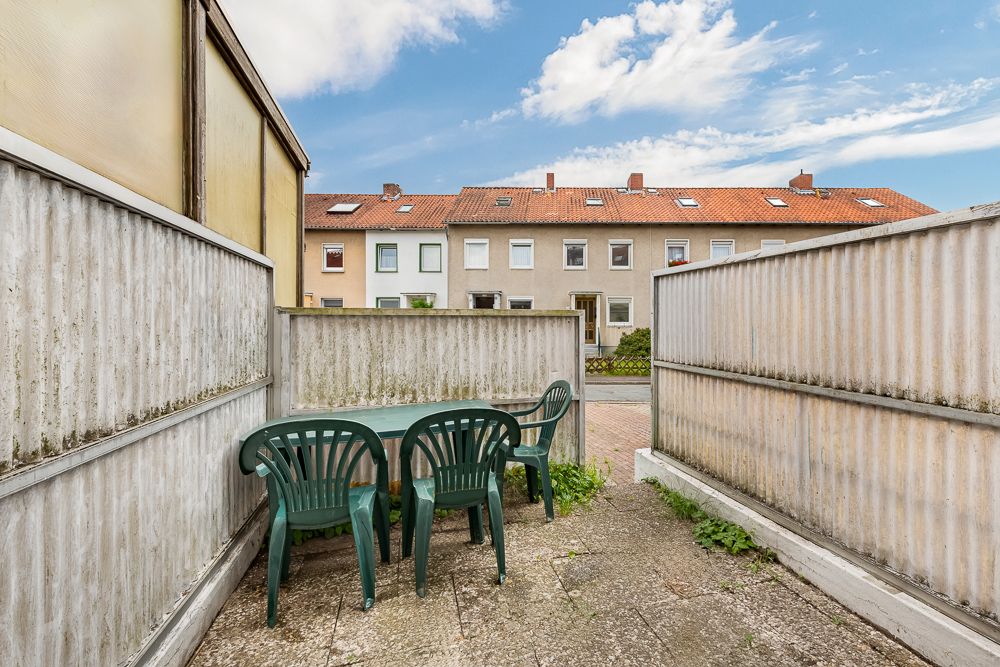 Kleine Terrasse mit vier grünen Plastikstühlen und Tisch, umgeben von grauen Wänden.