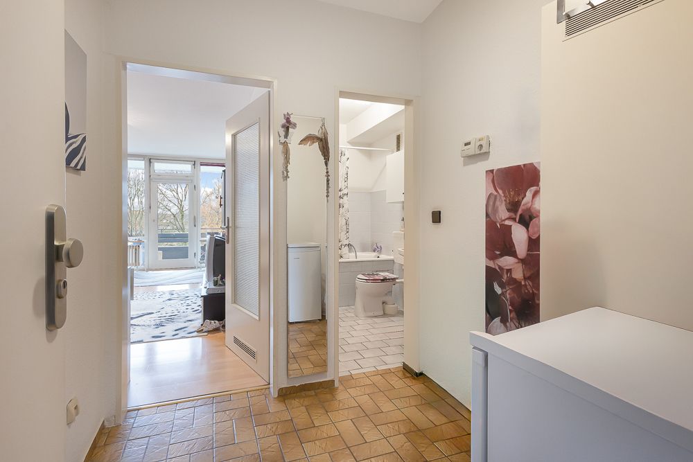 Flur mit Blick ins Wohnzimmer und Badezimmer, Fliesenboden und helle Wände.