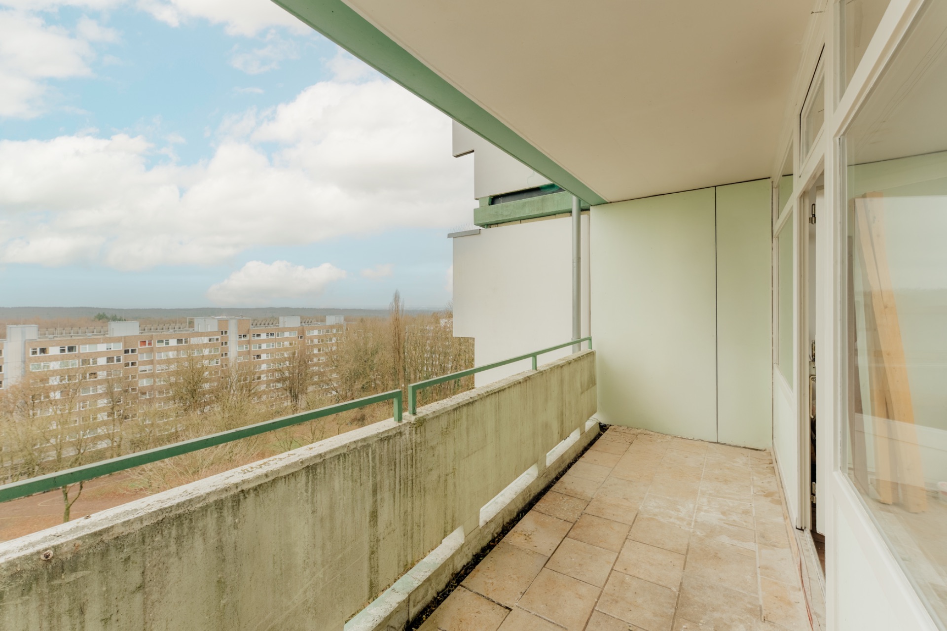 Geräumiger Balkon mit Fliesenboden und Blick auf Wohngebäude und Bäume.