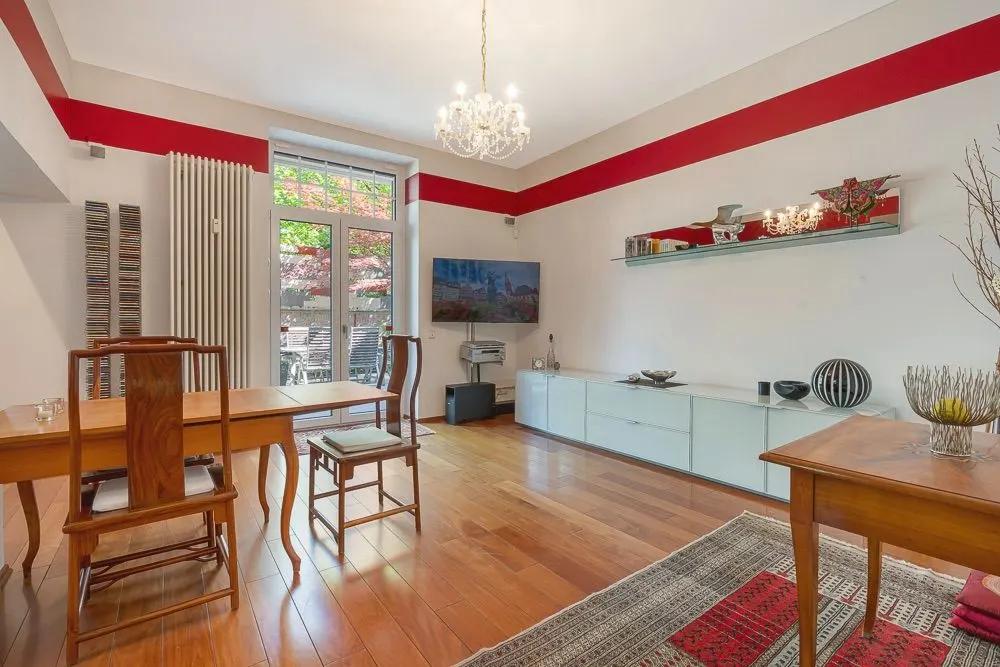 Wohnzimmer mit Holzboden, Esstisch, Stühlen, Sideboard, Regal, Fernseher und Kronleuchter.