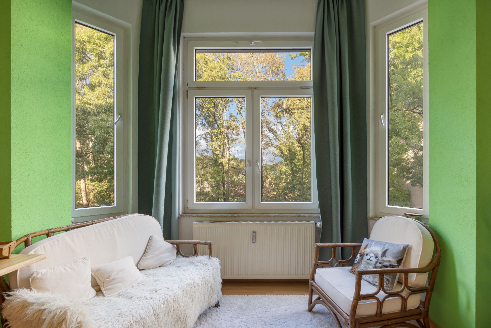 Heller Wohnraum mit grün gestrichenen Wänden, großen Fenstern, Sofa und Sessel.
