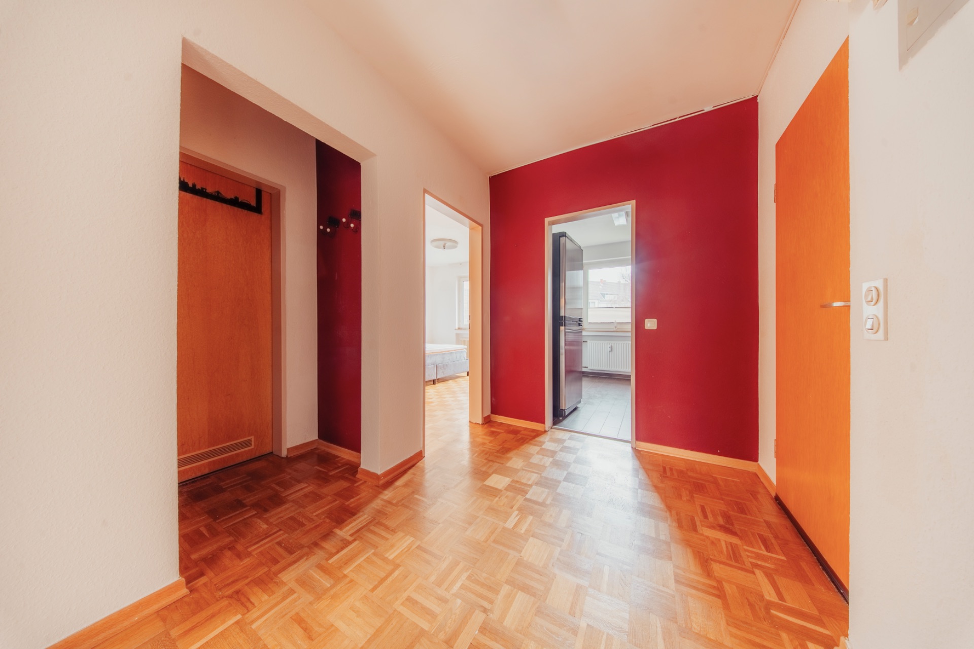 Heller Flur mit Parkettboden, roten Wänden und mehreren offenen Türen in verschiedene Zimmer.