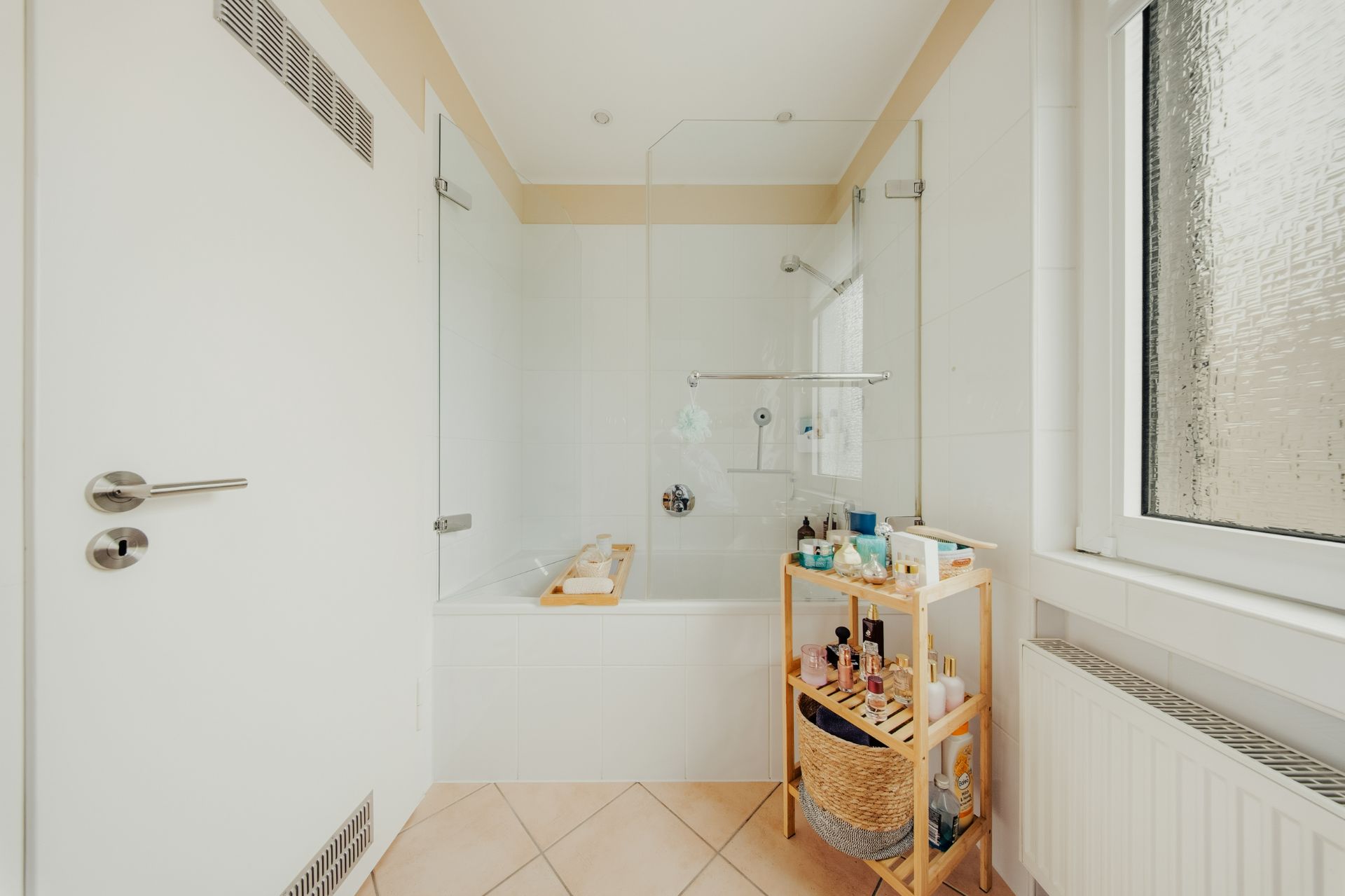 Helles Badezimmer mit Badewanne, kleinem Regal und Fenster mit Milchglas.
