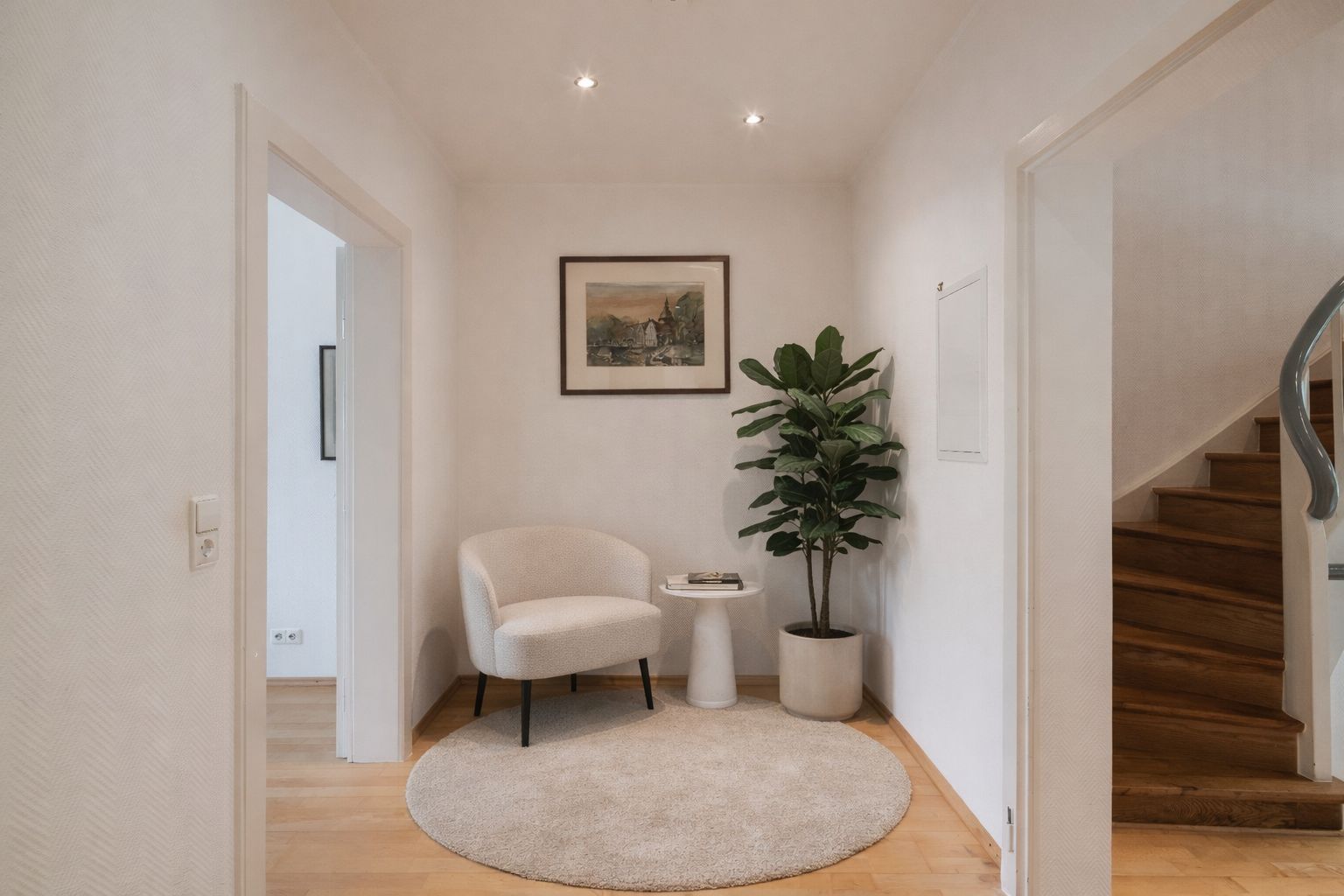 Heller Flur mit Sessel, rundem Teppich, Pflanze, kleinem Tisch und Bild an der Wand.