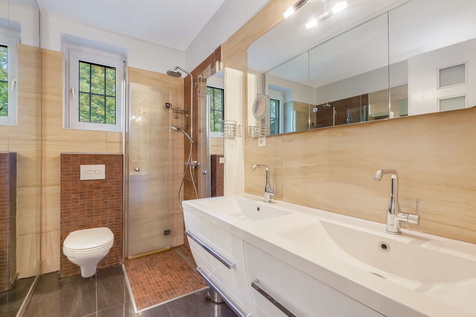 Modernes Badezimmer mit Doppelwaschbecken, großer Spiegelwand, Dusche und WC.
