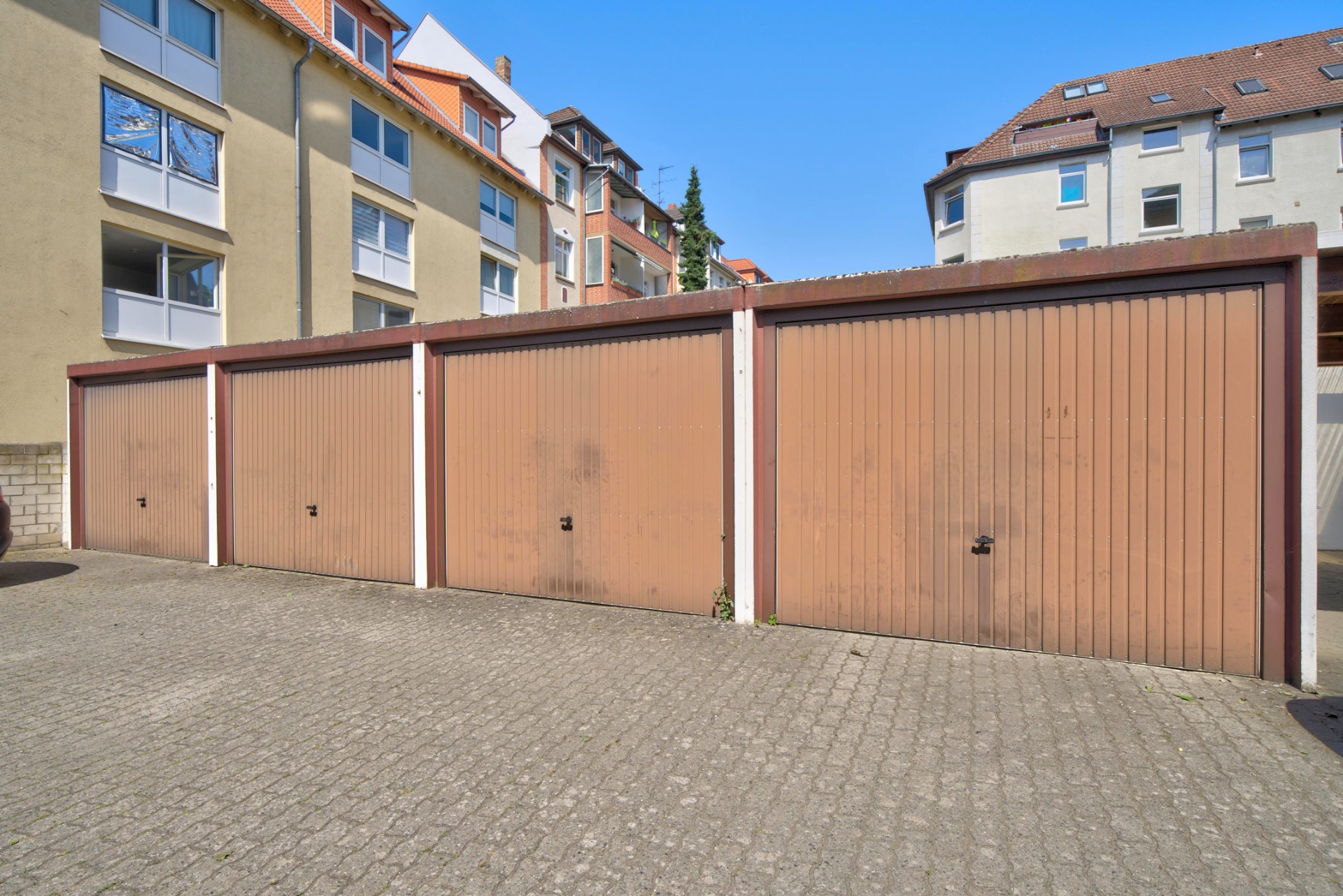 Vier braune Garagentore vor einem Mehrfamilienhaus bei Tageslicht.