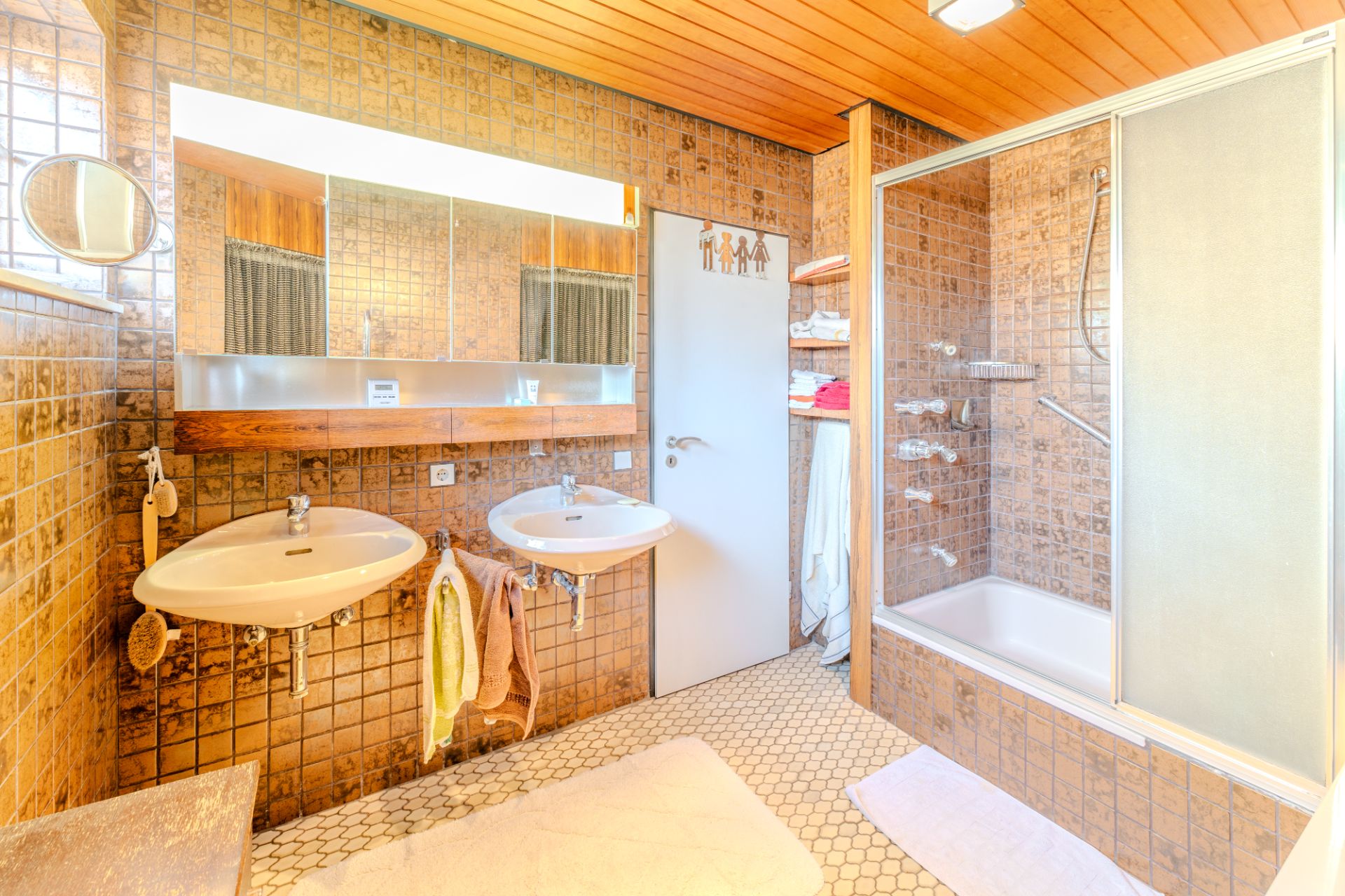 Helles Badezimmer mit zwei Waschbecken, Spiegel, Badewanne und braunen Fliesen.