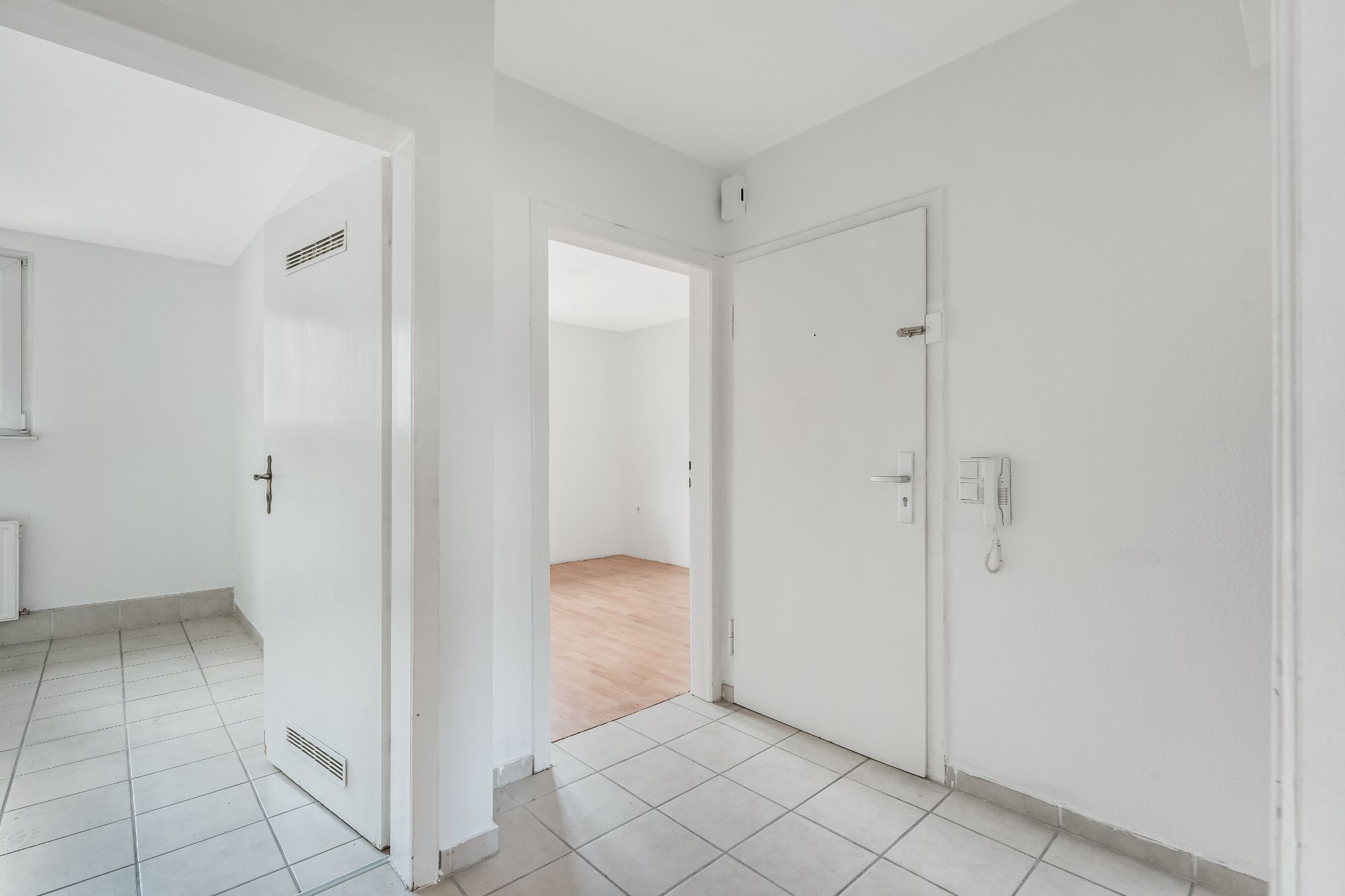 Heller Flur einer Wohnung mit weißen Türen, Fliesenboden und Zugang zu zwei Zimmern.