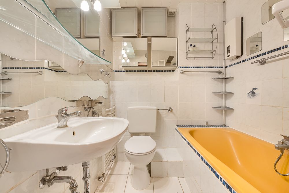 Helles Badezimmer mit gelber Badewanne, weißem Waschbecken, Toilette und Spiegeln.