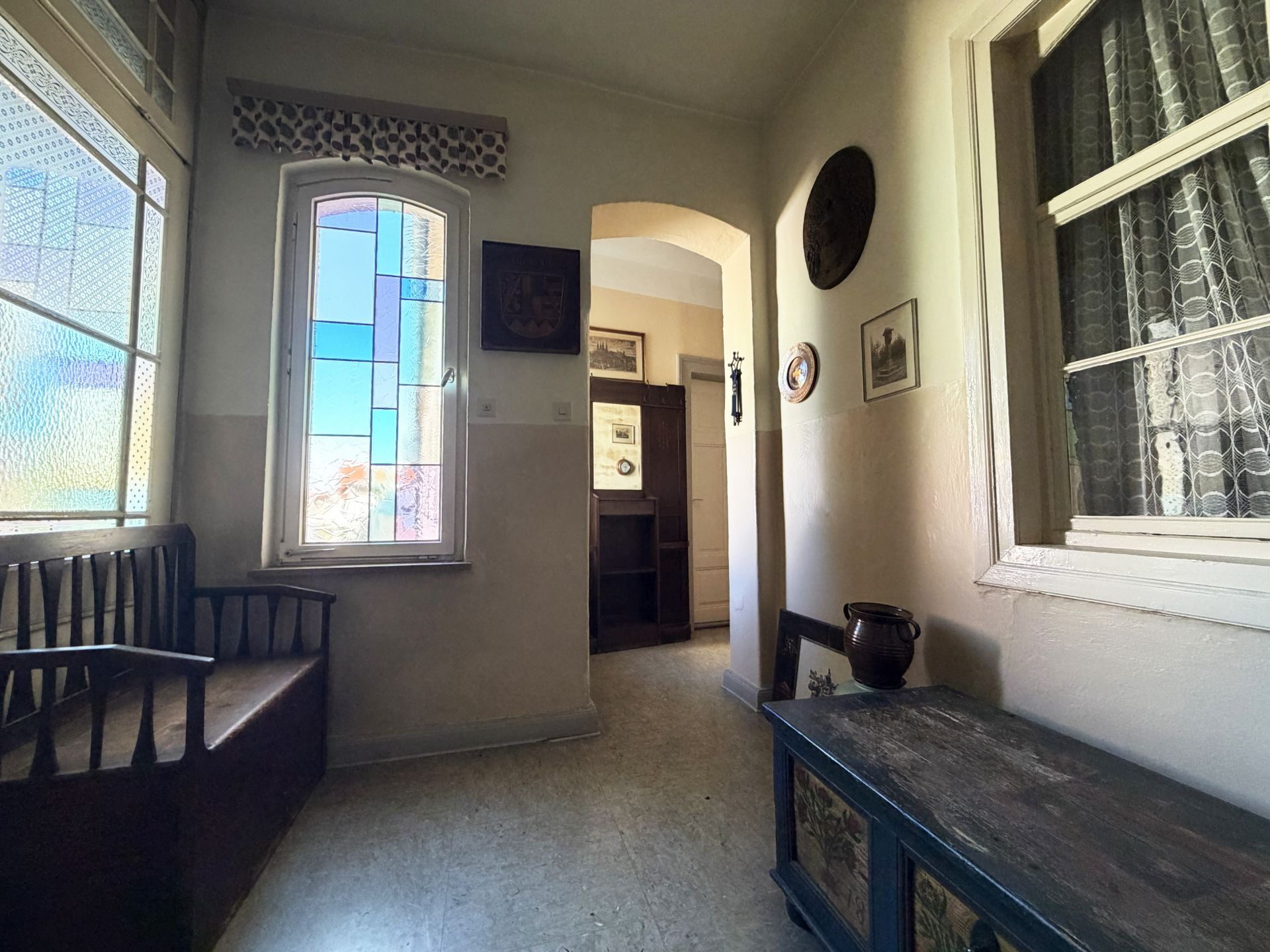 Heller Flur mit Holzbank, Truhe, buntem Fenster und Wanddekoration.