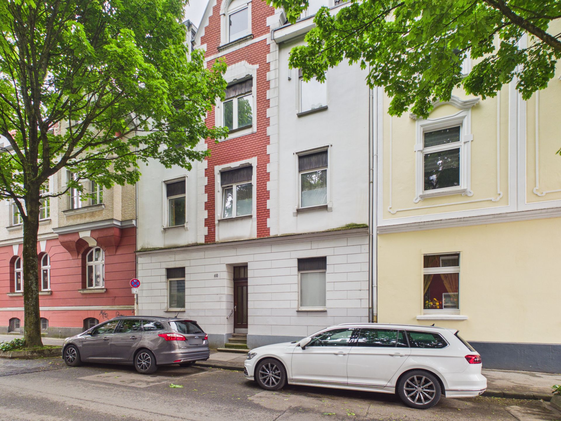 Mehrstöckiges Wohnhaus mit roter Fassade und parkenden Autos davor.