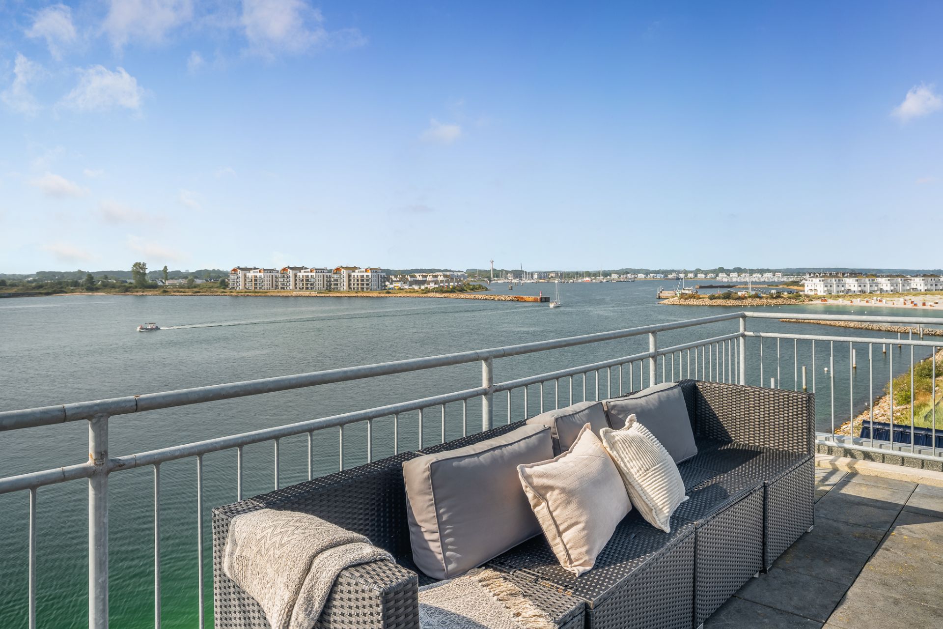 Sofa mit Kissen auf Terrasse mit Blick auf Wasser und ferne Gebäude.