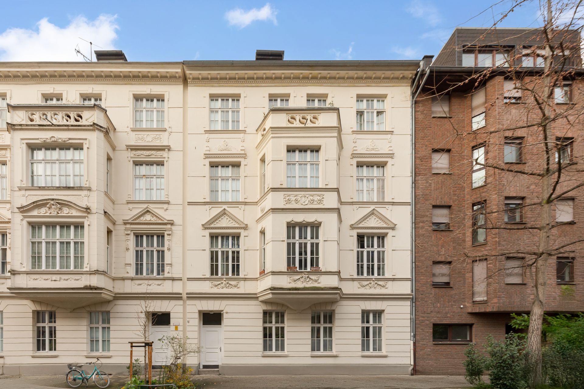 Fassade eines hellen, historischen Mehrfamilienhauses mit großen Fenstern und Verzierungen.