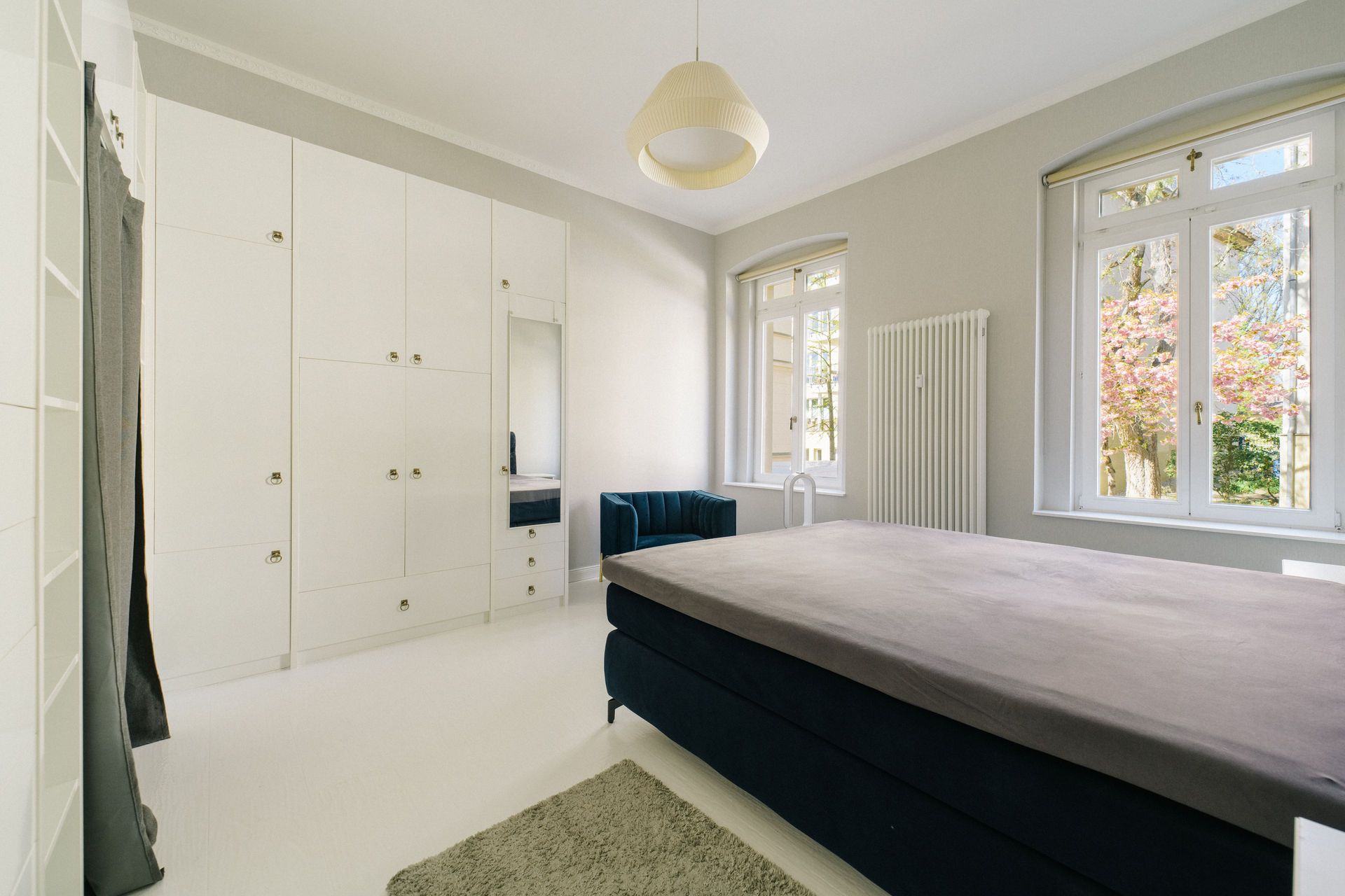 Helles Schlafzimmer mit großem Bett, weißen Einbauschränken, Teppich und zwei Fenstern.