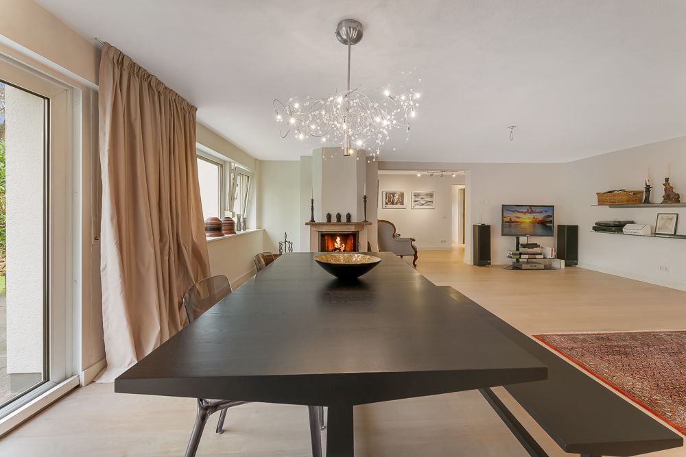 Großer heller Wohn- und Essbereich mit modernem Tisch, Kamin und dekorativem Kronleuchter.