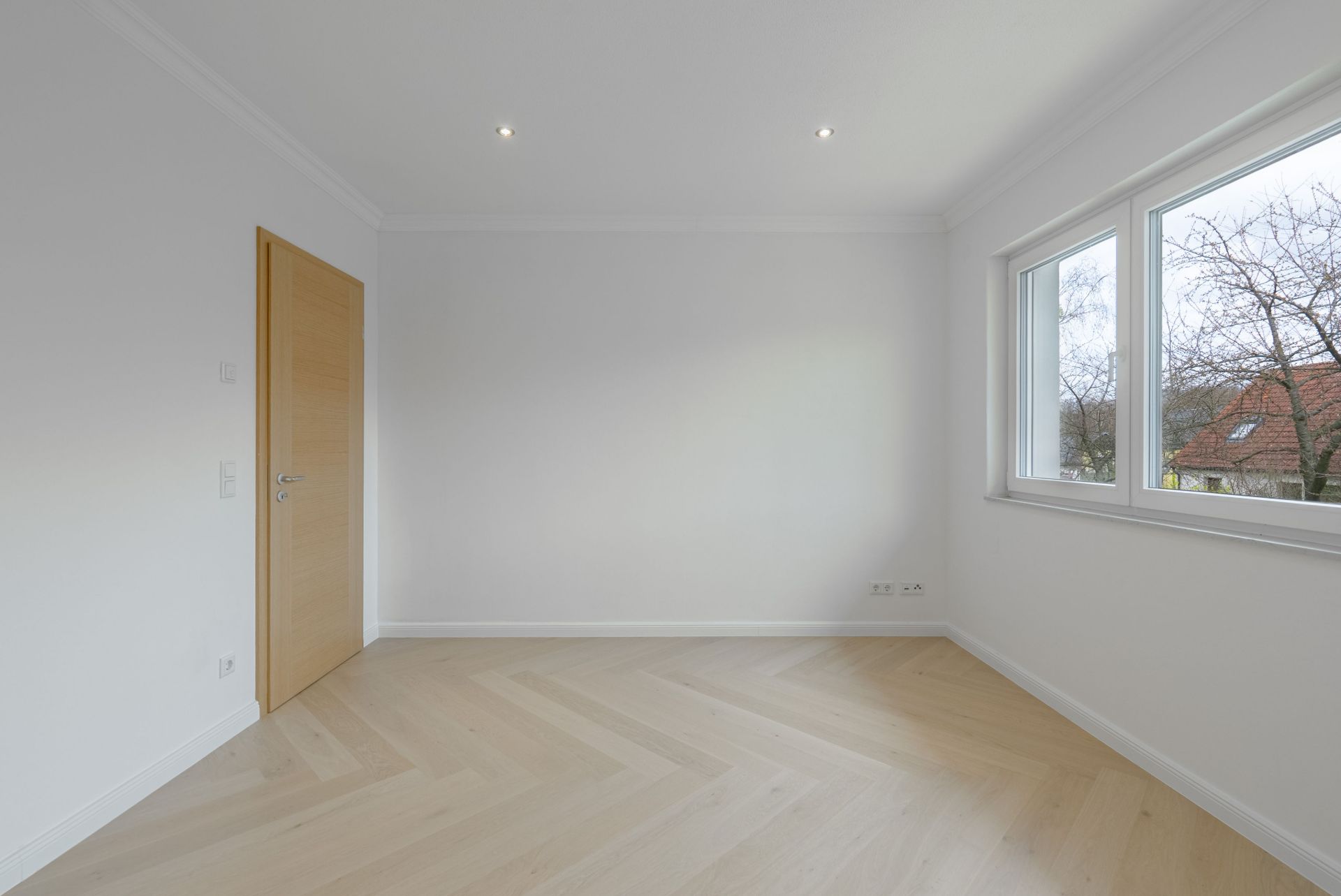 Leeres, helles Zimmer mit Holzfußboden, weißen Wänden, Tür und drei Fenstern.