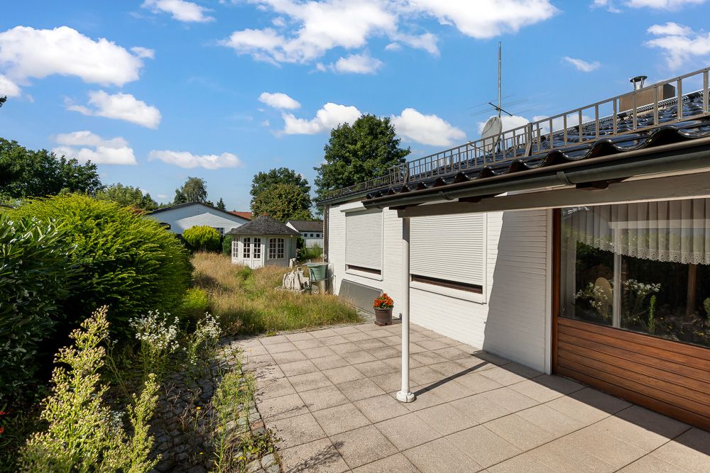 Gepflasterte Terrasse an einem Wohnhaus mit Garten und sichtbarem Gartenhaus im Hintergrund.