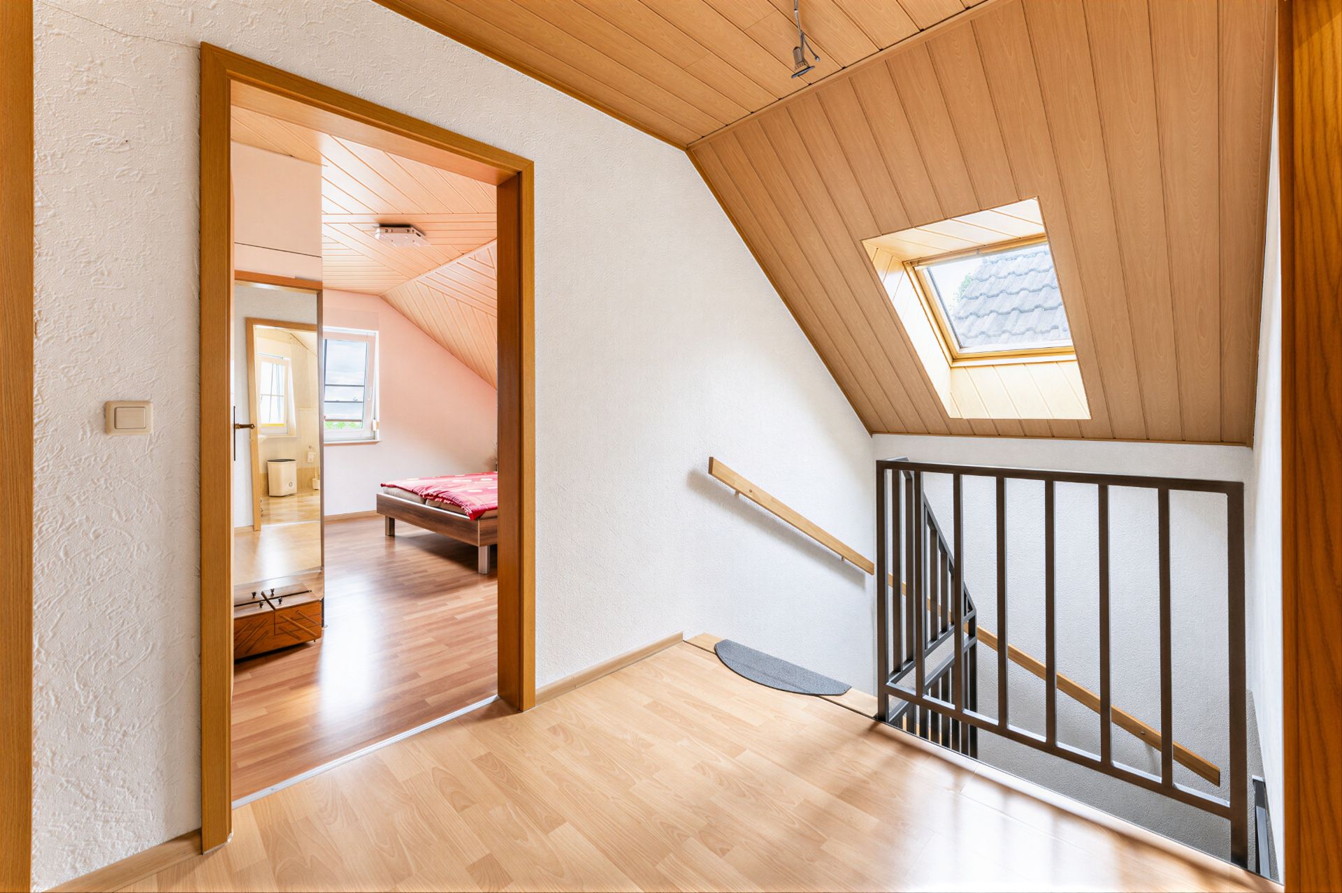 Heller Flur mit Holzdecke, Dachfenster und Zugang zu einem Schlafzimmer mit Bett.